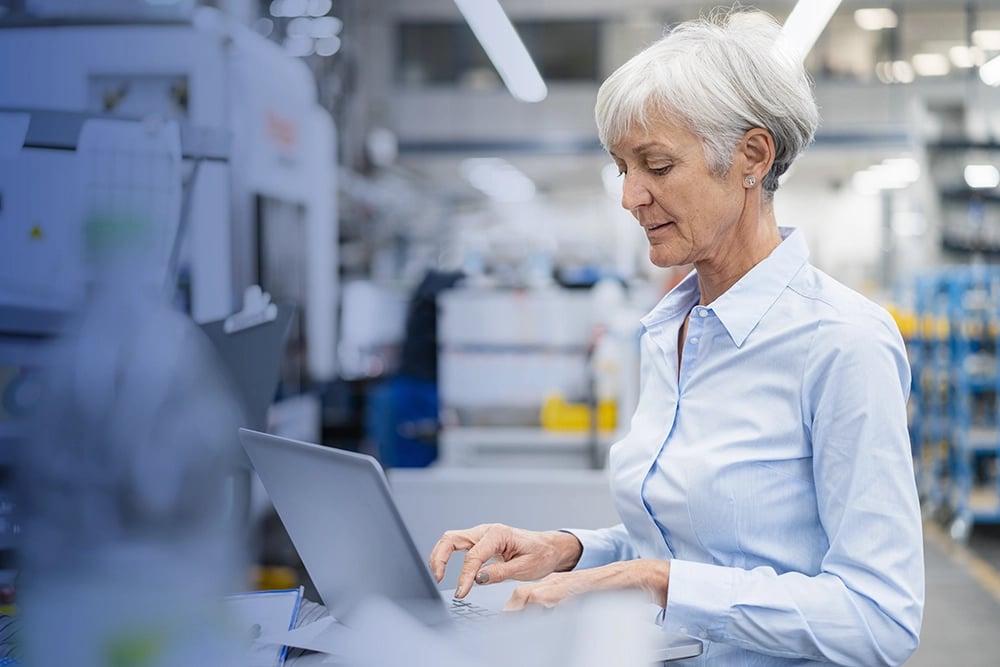 Femme mature dans une usine en train de rechercher des informations sur son laptop